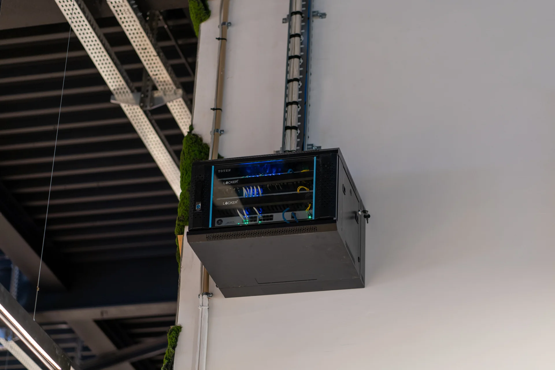 A wall-mounted network cabinet with switches and patch cabling, fed by cable trays from the ceiling.