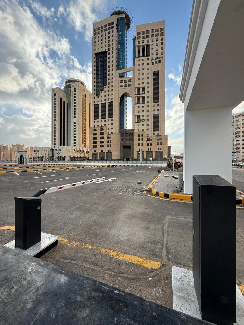 Tripoli Tower seen from the new car park: the twin towers above the parking lot, with an electronic barrier gate in the foreground.