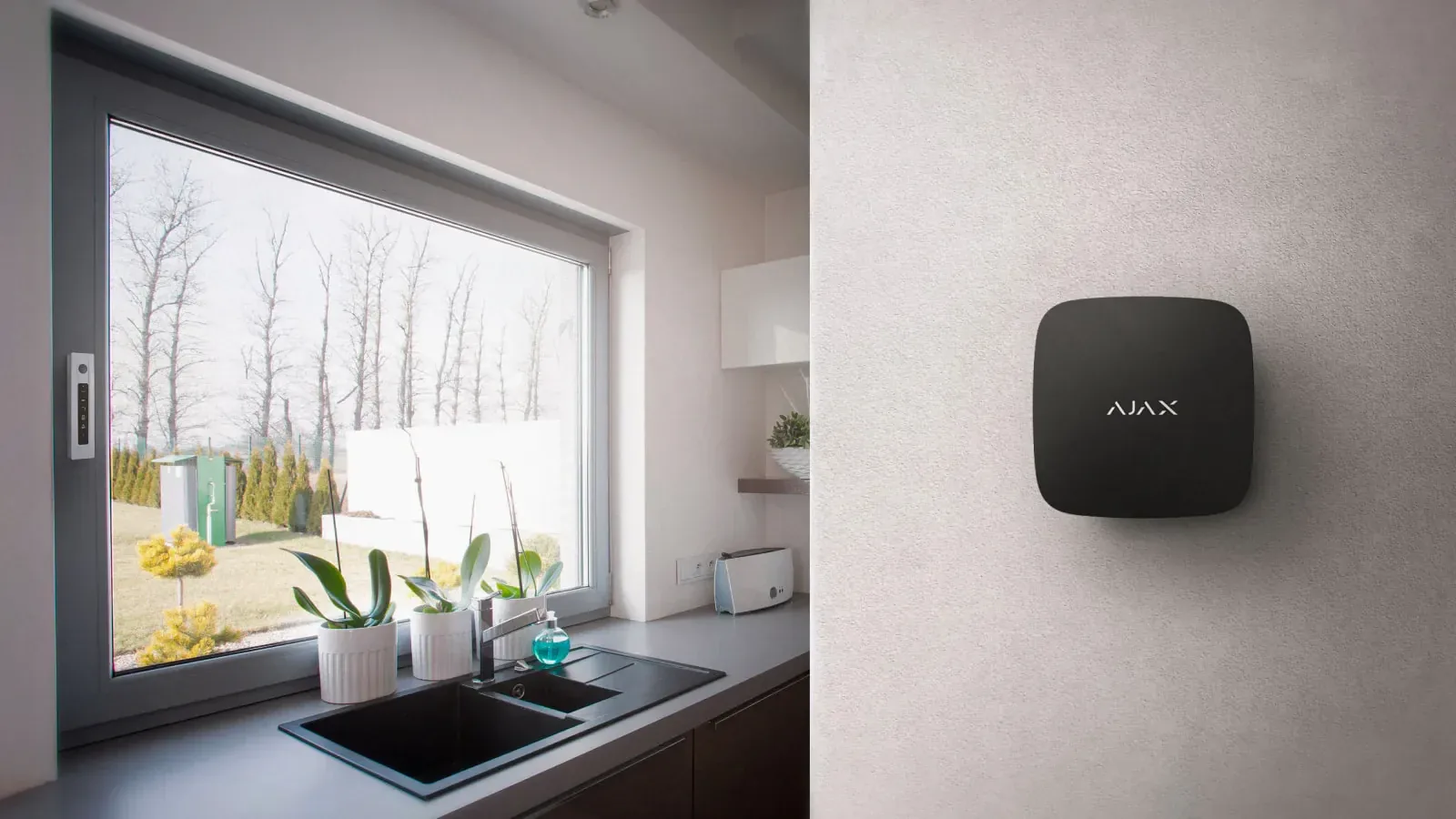 A smart-home alarm hub mounted on a wall beside a kitchen window.